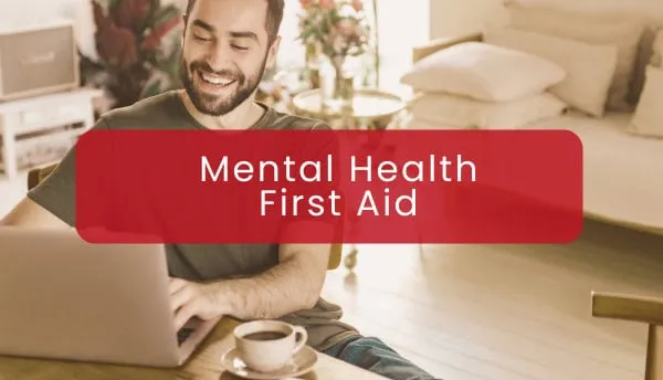 Smiling man using a laptop beneath a red banner reading Mental Health First Aid.