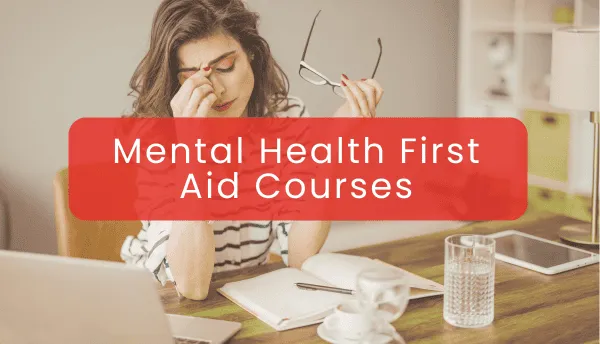 Concerned woman sitting at a desk with her laptop, taking off her glasses, with a title 'Mental Health First Aid Courses' overhead.